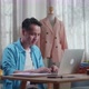 Asian Male Designer Working On A Laptop While Designing Clothes In The Studio - VideoHive Item for Sale