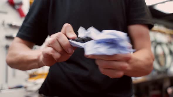 Crop man wiping metal bicycle detail with rag in garage alt