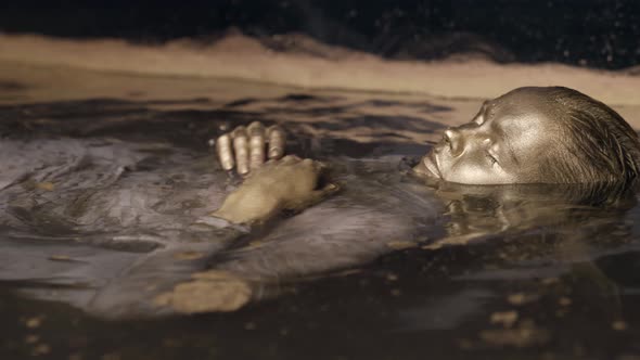 Ancient Goddess with Golden Skin Is Floating in Water Closeup Portrait of Female Face alt