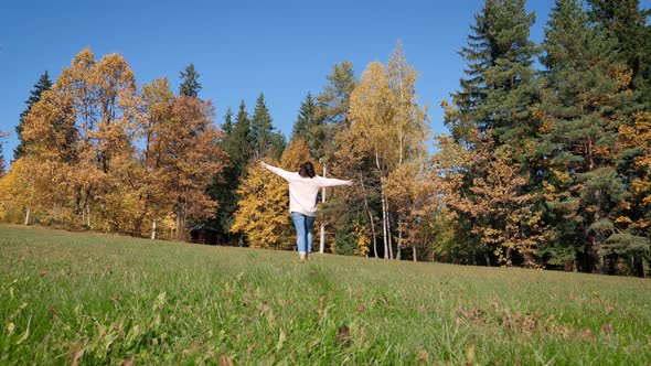 Woman Joyfully Running Across Green Lawn With Her Hands Raised To Side alt