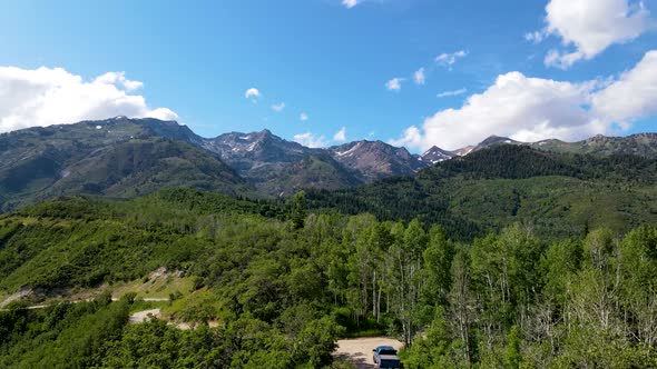 Pull back aerial view of a mountain road with a truck parked along the trail and rugged mountains in alt
