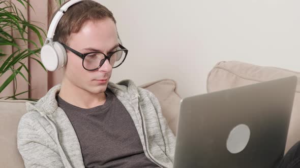 A Man in Glasses for Vision Works in Headphones Lying on the Couch in a Laptop