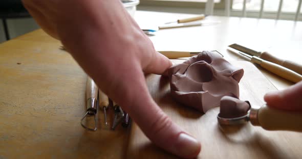 An artist carving and cutting brown modeling clay with a metal tool before sculpting and shaping the alt
