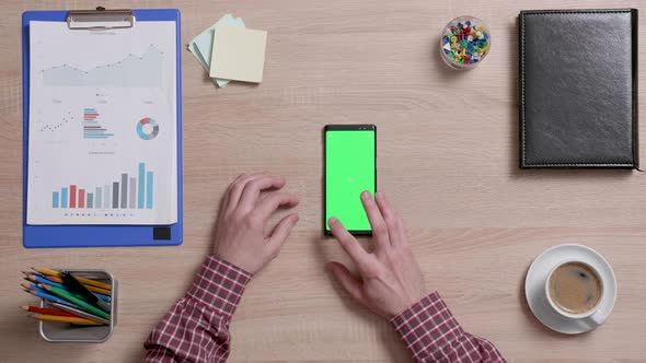 Top View of a Man's Hands Touch the Bottom Left Corner of a Green Screen on a Smart Phone alt