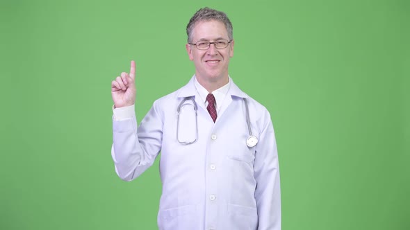 Portrait of Happy Mature Man Doctor Pointing Finger Up