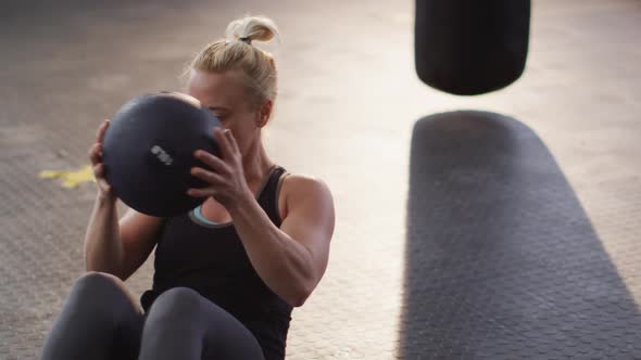 Fit caucasian woman performing abs exercise with medicine ball at the gym alt
