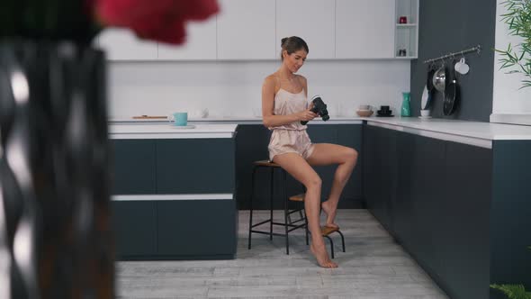 Girl Uses a Body Massager While Sitting in the Kitchen