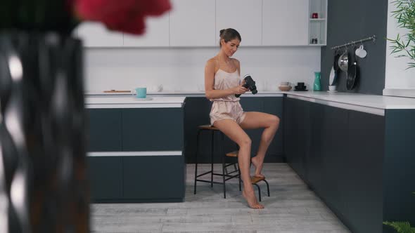 Girl Uses a Body Massager While Sitting in the Kitchen alt
