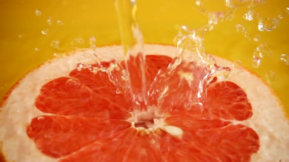 Half of a grapefruit in a jet of water on an orange background. Slow motion. alt