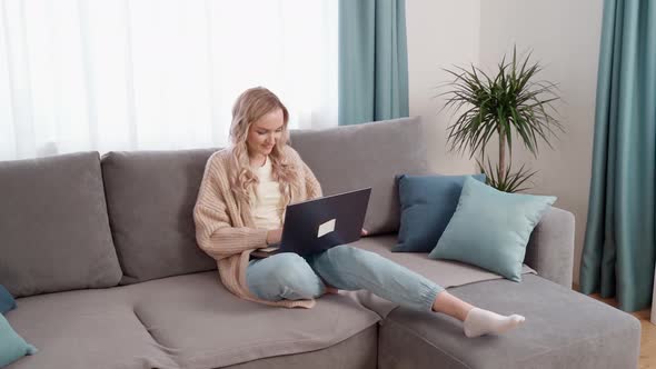 Blonde Girl Sitting on the Couch Working on a Laptop alt