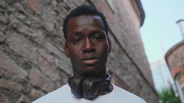 A Young Black Student with Headphones Walks Through the City Centre at Sunset