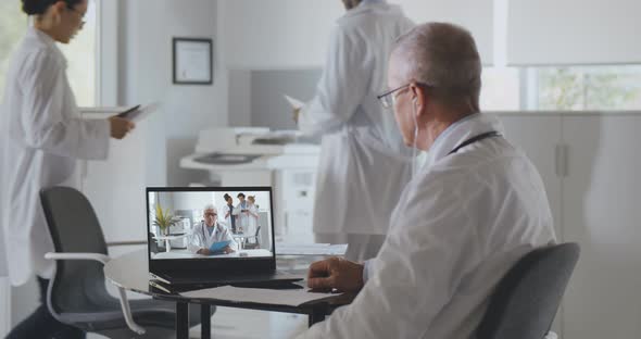 Mature Male Doctor Having Video Conference with Colleague Sitting in Clinic Office alt