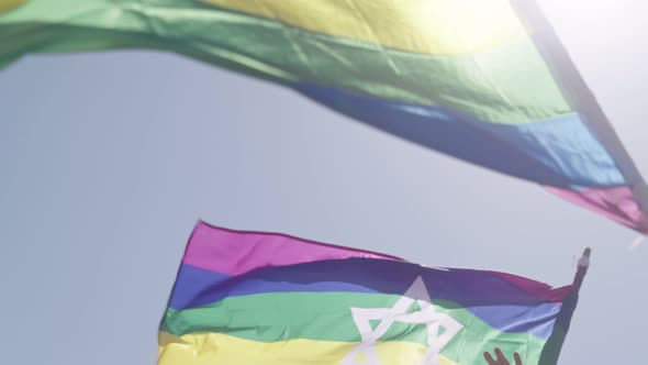 LGBTQ rainbow flags with a star of david waving in slow motion against the sun during a pride parade
