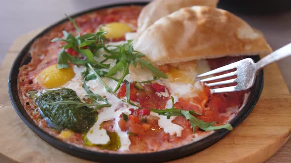 Eating Shakshuka Poached Eggs with Tomato and Bread Served in a Frying Pan