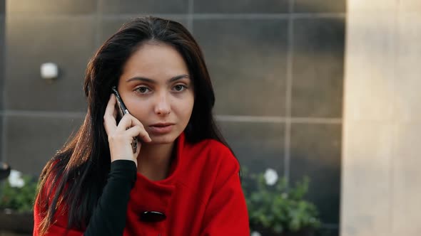 Young Business Lady Talking on a Cell Phone Sitting at a Table in a Cafe on the Street