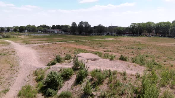 drone shot of a undeveloped vacant lot on the edge of a dutch city, with a skyline in the background alt