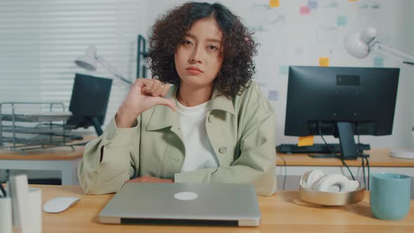 Unhappy Asian Businesswoman looking at camera and Doing Thumbs Down