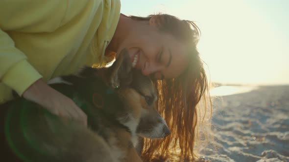 Beautiful Happy and Affectionate Laughing Girl in Yellow Hoodie at Summer Beach with Cute Pet Corgi alt