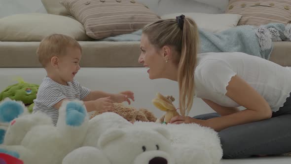 Happy and smiling mom with baby playing in living room at home with plush stuffed animals toys