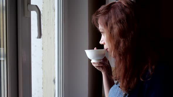 Young Woman Drinks Coffee Looking Out the Window During Quarantine. Social Distancing