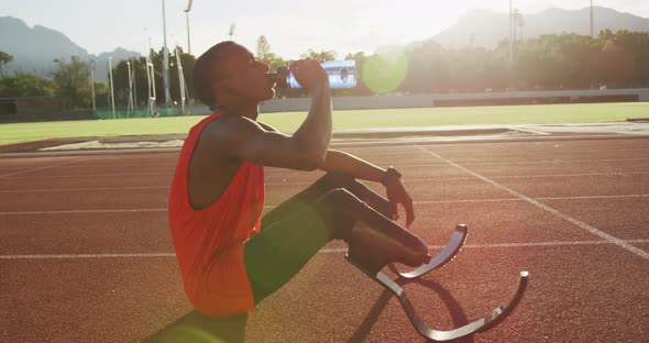 Disabled mixed race man with prosthetic legs sitting on racing track alt