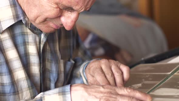 An elderly Caucasian man over 70 years old looks at a photo album while sitting at a table at home.  alt