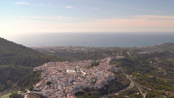 Right pan across whitewashed village on top of hill with ocean in distance alt