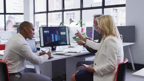 Diverse business people sitting using computer and takling at desk in office alt