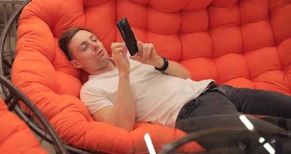 Man Looking at Photos on the Phone While Lying on the Couch