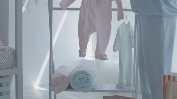 Unrecognizable Caucasian Pregnant Woman Hanging Children Clothes on Hanger in Future Baby Room alt