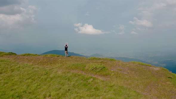 Aerial Drone View. Flying Around Young Man Standing on Top of the Mountain at Sunset V2 alt