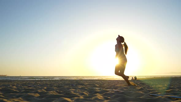 Women players play beach volleyball and a player jump serves serving the ball. alt