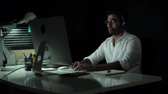 Businessman working night shift wearing microphone headset talking with customer in call center
