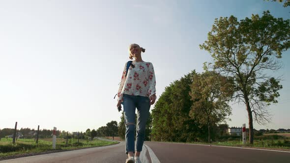 Woman with Backpack Walking on Countryside Road. alt