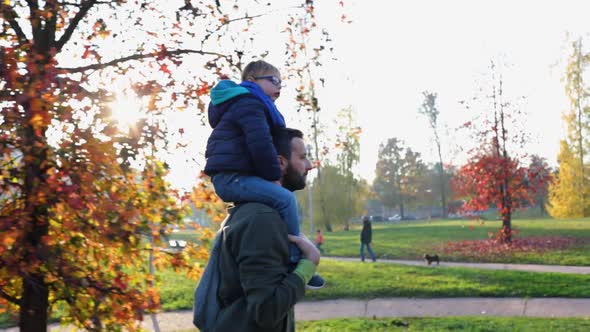 Father Walking in Urban City Park with Son on Shoulders