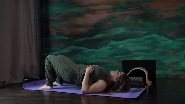 a Woman in a Green Jumpsuit is Lying on a Sports Mat alt
