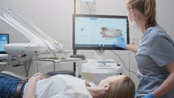 Girl Doctor Dentist Demonstrates a 3D Model of Teeth on a Touch Monitor alt