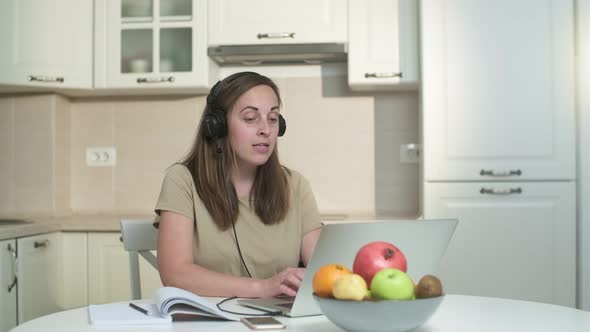Young woman in headphones working on a laptop in the kitchen. alt