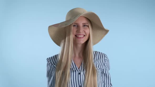 Beautiful Smiling Girl Putting a Hat on Her Head on Blue Background alt