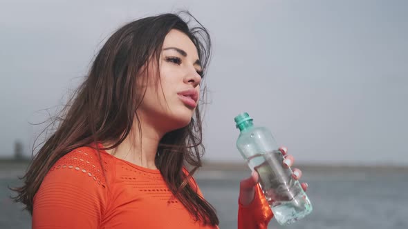 Athletic fitness woman, sportswoman drinks water. Attractive sports girl drinks water on the street alt