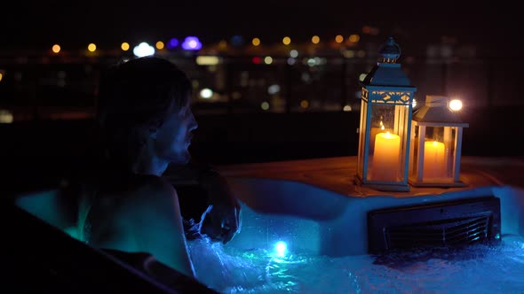 A Young Man is Relaxing in the Hot Tub on a Rooftop at Night alt