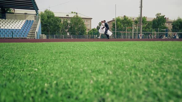 Bride and Groom are Running Along the Treadmill at the Stadium the Green Grass alt