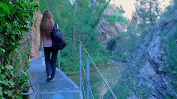 Woman is Crossing a River on a Hanging Bridge with a Backpack