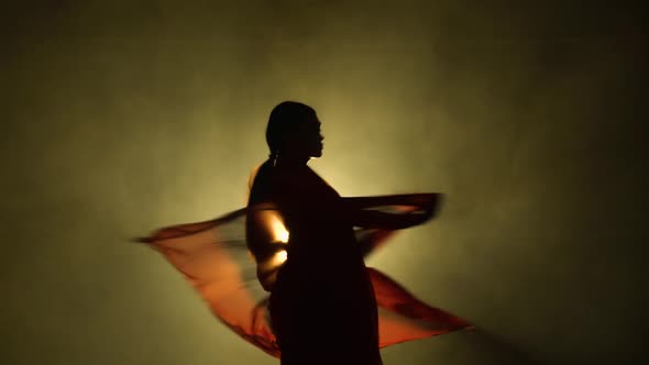 Silhouette a Young Girl Dancer in a Red Sari. Indian Folk Dance. Shot in a Dark Studio with Smoke alt