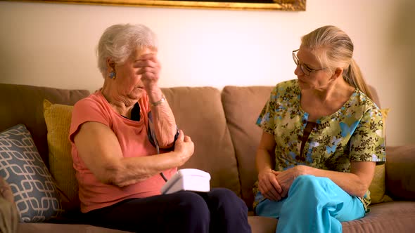 Home healthcare nurse and elderly woman taking blood pressure with a monitor. alt