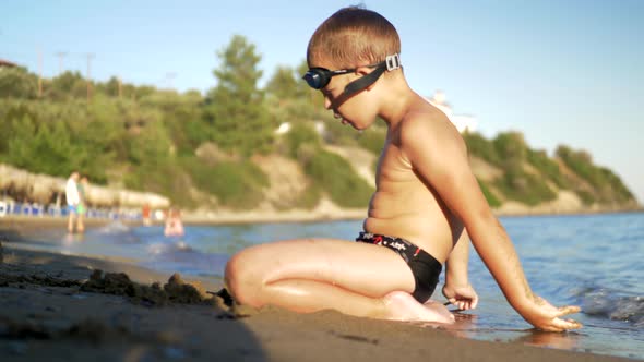 Child sitting on the sand and enjoying sea waves washing him alt