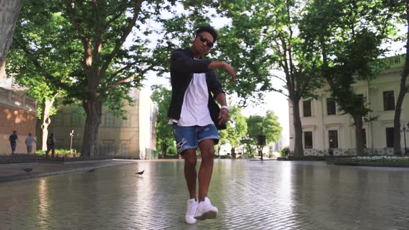 Young Stylish Hipster Black Man in White Headphones and Sun Glasses Dancing Outdoor in City Centre alt