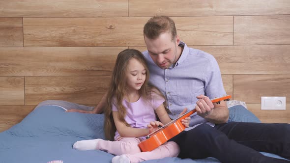 Young Caucasian Dad Teaching Guitar and Ukulele to His Daughter Learning