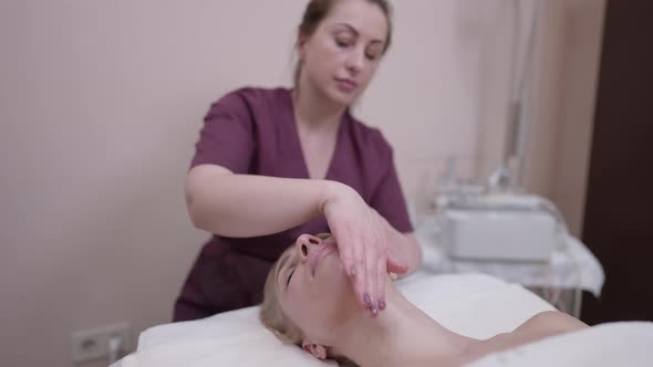 Relaxed Woman Enjoying Face and Neck Massage in Beauty Spa As Blurred Masseur Touching Rubbing Skin alt