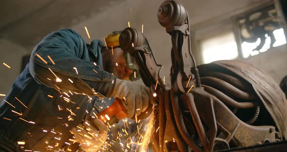 Locksmith Cuts and Sands the Decorative Metal Steampunk Fish Sculpture By Electric Grinder with a alt